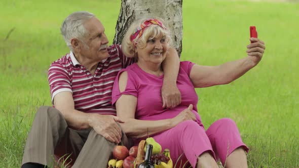 Family Weekend Picnic. Senior Old Grandparents Couple in Park Using Smartphone and Makes Selfie