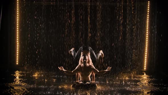 Exciting Acrobatic Show in the Rain. Three Men Posing Against a Black Studio Background Backlit 