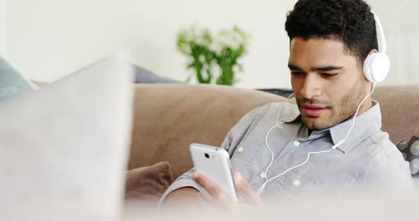 Happy man listening music on mobile phone in living room