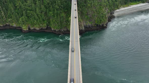 Top down drone shot tracking a car across a bridge over the ocean.