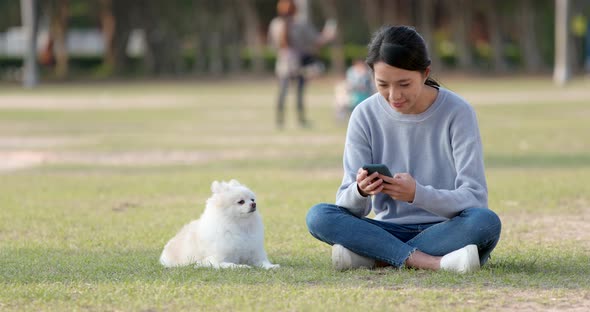 Woman play with her dog and sitting at the green lawn with using cellphone