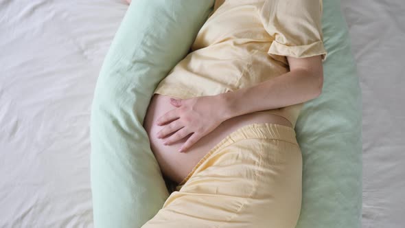 Closeup Of Pregnant Woman Belly And Maternity Pillow In Bed