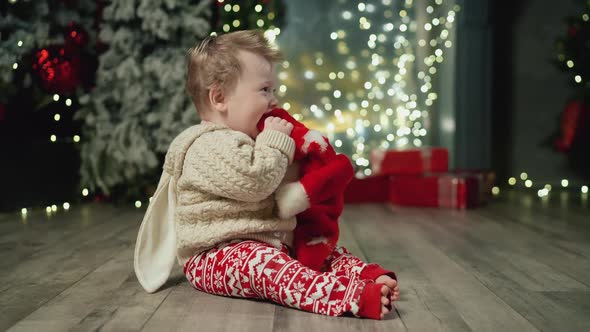 Joyful Baby in Rabbit Sweater Plays with Red Hat Drums Feetand and Enjoys New Year