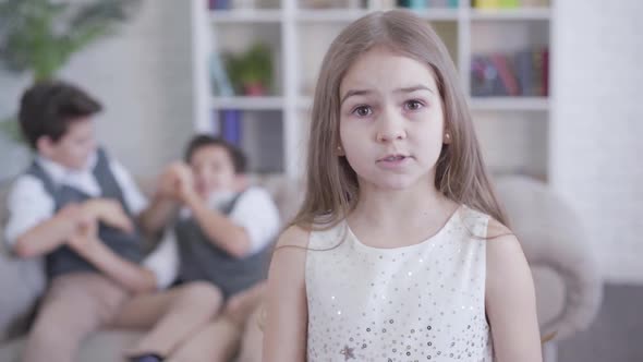 Portrait of Pretty Little Caucasian Girl Turning To Camera and Shaking Head As Blurred Boys Fighting