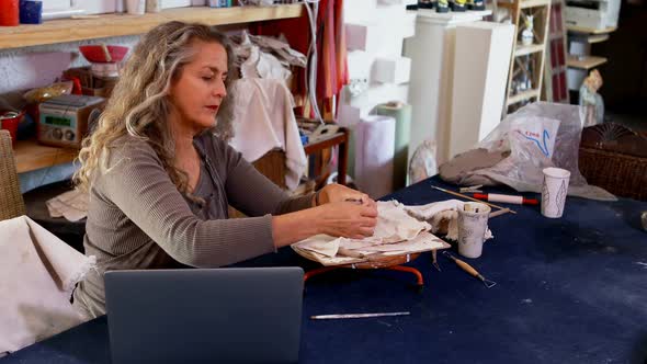 Mature female potter molding a clay while using laptop