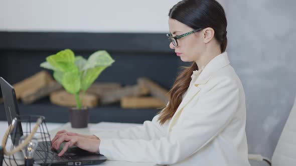 Side View of Concentrated Young Slim Woman Typing on Laptop Keyboard and Taking Off Eyeglasses