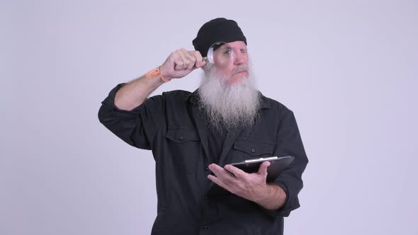 Mature Bearded Hipster Man Holding Clipboard While Using Magnifying Glass