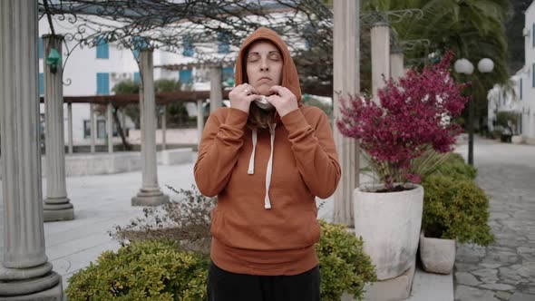 Woman in orange sweater removes medical mask and breathes on empty street.