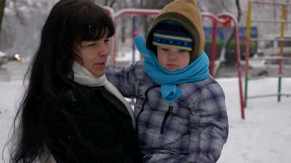 Young Beautiful Mother And Cute Child Walk Outdoors During Snowfall. Winter City 7