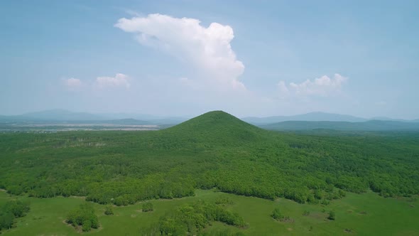 Aerial View of an Endless Geen Meadow and a Hill Against the Blue Sky with Clouds