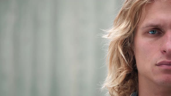 Close up of the attractive male hipster, half face of blue-eyed guy with blond long curly hair