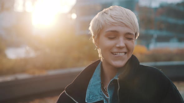 Portrait of Young Caucasian Woman with Short Blond Hair Winking in the City Park