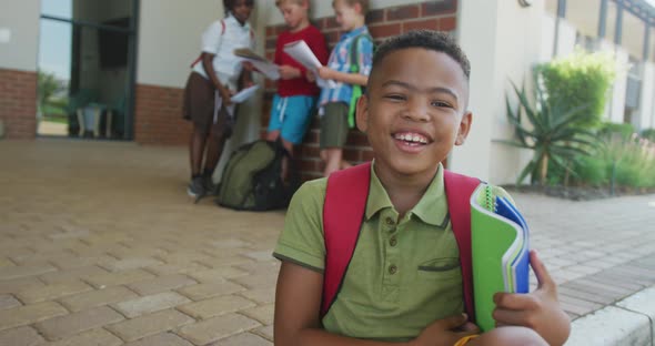 Video of happy african american boy holding books in front of school