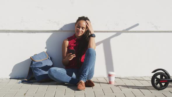 African american woman sitting and using smartphone on promenade by the sea