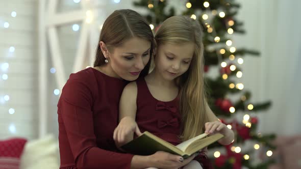 There are a little girl and her mom on the foreground. They are reading a book together. On the back