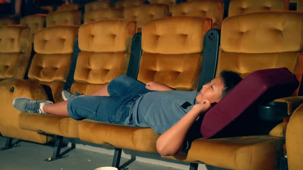 A Boy Laying Down on Armchair in Cinema