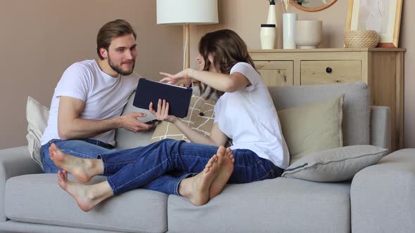 Happy young couple, woman showing her boyfriend something on a digital tablet while a young man