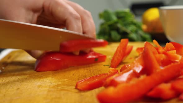 Closeup of a Woman's Hands with a Knife Cutting Red Bell Peppers on a Kitchen Board