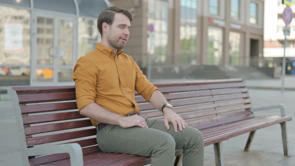 Young Man having Back Pain while Sitting on Bench Outdoor