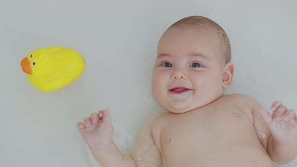 A Baby Girl Bathes in a Bath with a Toy. Closeup.
