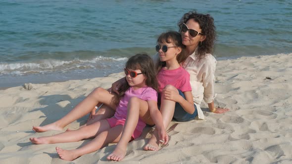 The family is sitting on the sand on the beach. 