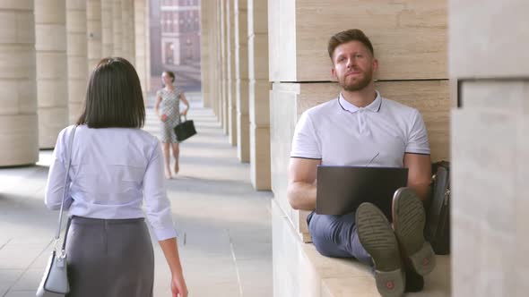 Tired Young Businessman Sitting Outdoors at City Street Working on Laptop