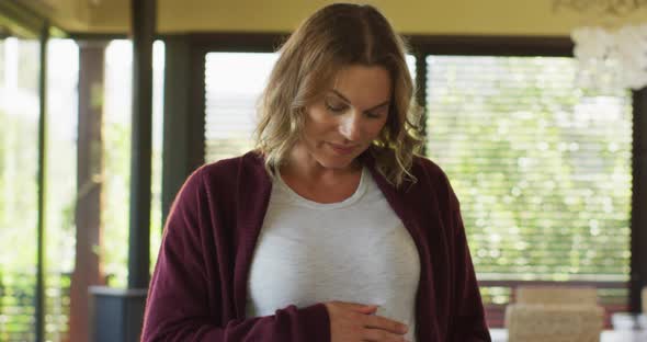 Portrait of happy caucasian pregnant woman touching belly and looking at camera