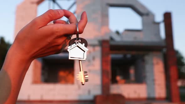 Hand with the key to the future house on the background of a construction site and walls