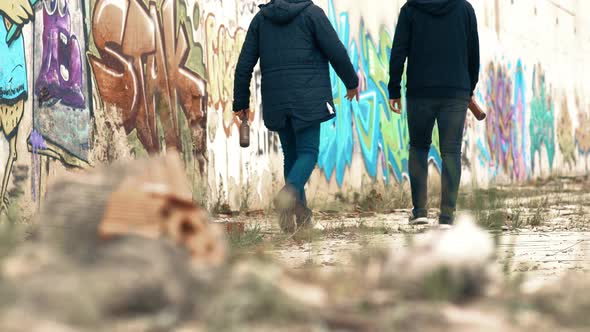 Young people drinking alcohol breaking bottles in front of graffiti.