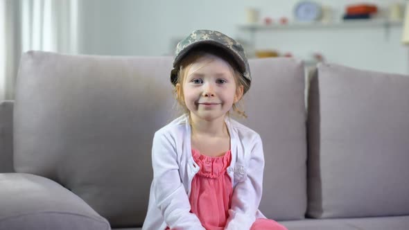 Funny Smiling Preschooler Girl in Military Cap Sitting on Sofa, Little Patriot