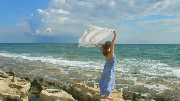 Attractive Woman Holding White Scarf in Wind on Rocky Shore. Freedom, Happiness