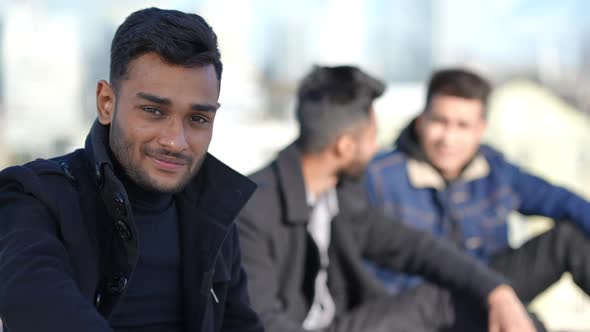 Portrait of Handsome Young Man Looking at Camera Smiling As Blurred Friends Talking at Background