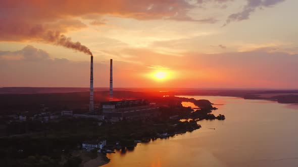 Factory chimneys with smoke. Beautiful sunset over river.