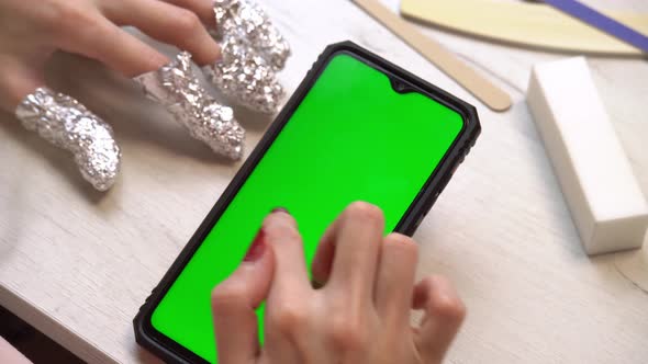 A Girl During a Manicure Uses a Smartphone with a Green Screen