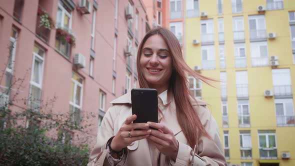 A Young Girl Walks Through a Residential Area and Surfs the News on Her Phone