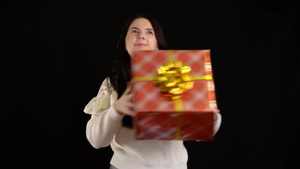 Young Woman with a Gift Box on Black Background. Gift Box with White Ribbon for Happy New Year