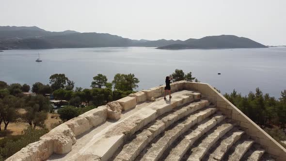 Beautiful girl walking in an antique Amphitheater with sea view in Kas, Turkey. Drone angle.