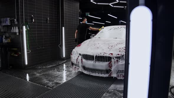 Man Washes Car Covered with Foam Using a Sponge
