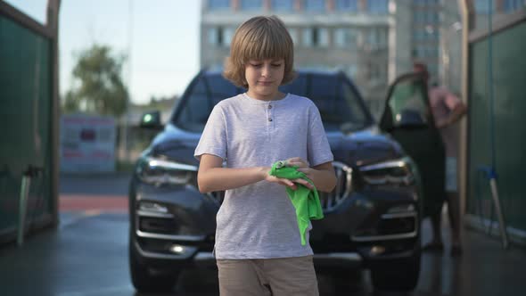 Boy Cleaning Hands Standing at Blurred Black Vehicle with Man Walking at Background