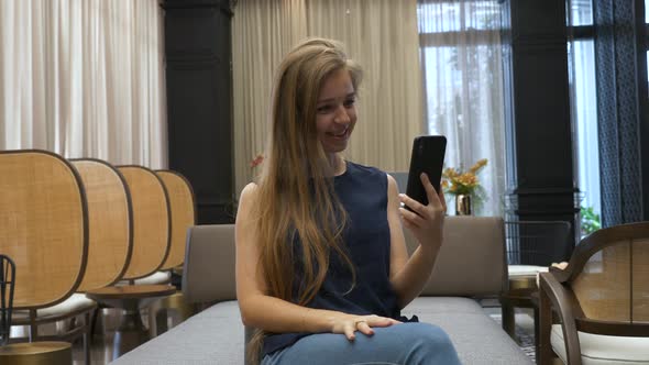 Happy Beautiful Young Girl Sitting on Couch and Making Video Call on Phone