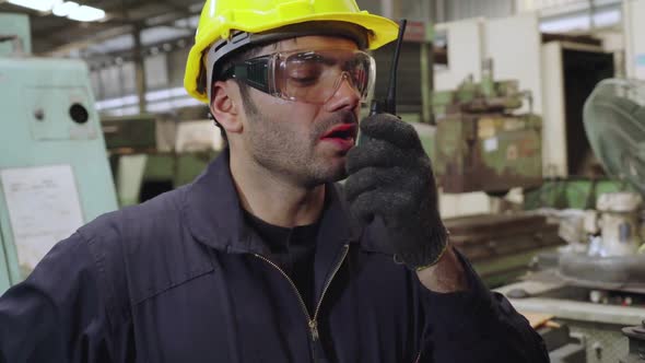 Factory Worker Talking on Portable Radio While Inspecting Machinery Parts