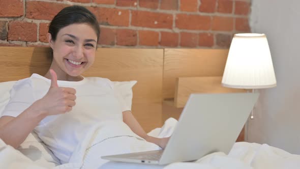 Young Indian Woman with Laptop showing Thumbs Up in Bed