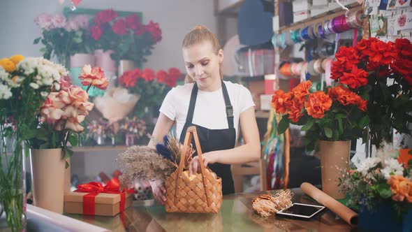 Young Florist Female Decorates a Bouquet of Dried Flowers in a Wicker Basket Cheerful Woman Working