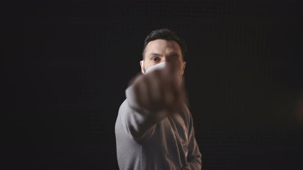 Young Man with Face Mask Posing Against Black Background. Man with Mask Raise Hand and Points with