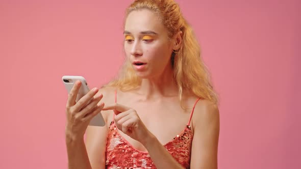 Closeup of Anxious Young Woman Looking at Phone Seeing Bad News Over Pink Wall