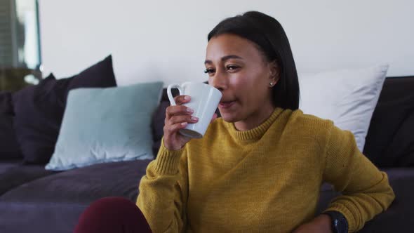 Mixed race woman sitting on floor drinking a cup of coffee