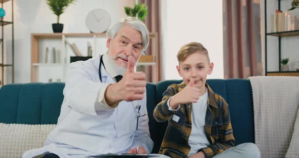 Bearded Pediatrician Looking Into Camera with Smiling Teen Boy Patient and Gesturing Thumbs Up