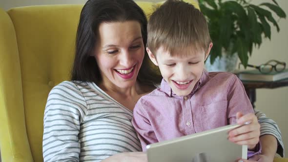 Happy Family of Mom and Son Use Tablet and Have Fun Sitting in Apartment During Isolation Spbd