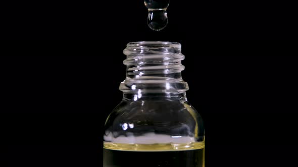 Cosmetic Oil Drips From a Pipette Into a Glass Bottle Against a Background of Black Background