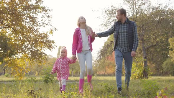 Handsome Caucasian Man Strolling with His Two Daughters Dressed in Pink Clothes in the Autumn Park